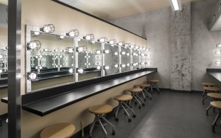 Dressing room area with multiple chairs, vanity mirrors, and lights. 