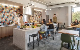 Kitchen area with people sitting at high-top stools and preparing food.