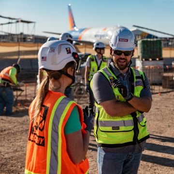 Two people having a discussion at an airport jobsite with planes in the background