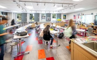 Students enter a classroom with bright lights and large windows on the far wall.