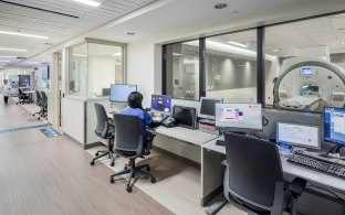 Desks and chairs with computers looking into large glass windows with medical imaging equipment