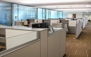 An office space with cubicle desks in the middle and private offices on the side of the room.