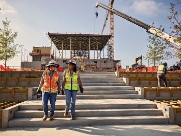 Two people walking down an outdoor staircase on a jobsite. 