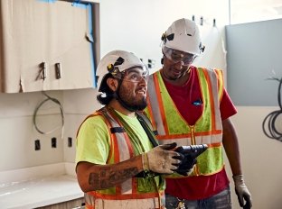 Two people collaborating and looking at a tablet while wearing PPE.